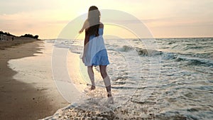 SLOW MOTION: Girl running in shallow water at sunset. A girl in a white dress is running at the water`s edge near the