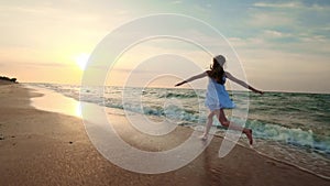 SLOW MOTION: Girl running in shallow water at sunset. A girl in a white dress is running at the water`s edge near the