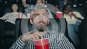 Slow motion of grey-haired man chewing popcorn watching scary movie in cinema