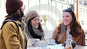 Slow motion. Group of friends talking, laughing on a coffeeshop terrace. Three young adult people having a friendly
