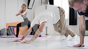 Slow motion group practicing yoga in yoga studio, man in focus standing in Downward facing dog pose