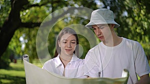 Slow motion. A guy and a girl are holding an unfolded map in their hands and arguing which way they need to go, standing