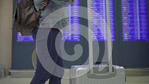 Slow motion - Happy Asian woman looking at information board checking her flight with luggage in terminal hall.