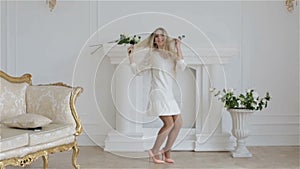 Slow motion. The happy beautiful girl in white fashionable dress is jumping in a studio against a white wall.