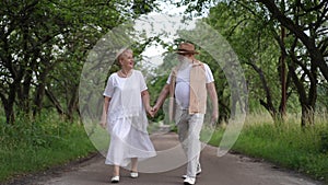 Slow motion. A happy elderly married couple walks along a path in a city park outdoors and cheerfully jumped, holding