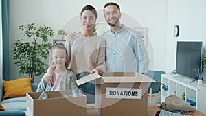 Slow motion of happy family mother father and child standing near donation boxes with clothes at home