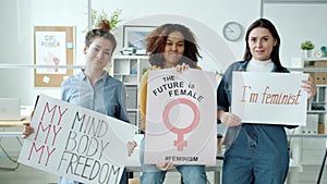 Slow motion of happy feminists standing with posters smiling looking at camera indoors