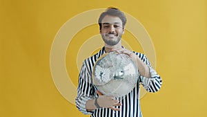 Slow motion of happy Indian guy dancing holding disco ball on yellow background