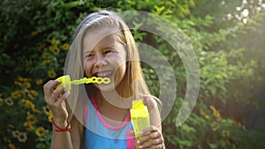 Slow motion of a Happy little caucasian girl blowing soap bubbles in on a sunny day. Concept happy childhood or children