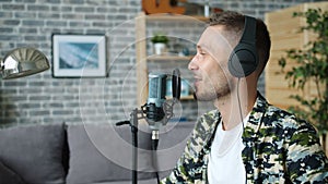 Slow motion of happy man in headphones talking in microphone in recording studio