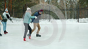 Slow motion of happy men and women enjoying ice-skating in winter park holding hands laughing