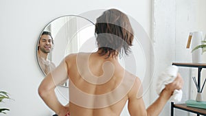 Slow motion of happy mixed race man danicng in bathroom with towel looking at mirror on wall