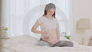 Slow motion Happy Pregnant Woman sitting on bed holding and stroking her big belly at home,Pregnancy of young woman enjoying with