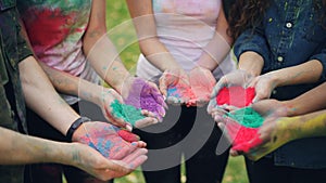 Slow motion of human hands holding multicolor powder paint gulal for Holi festival ceremony standing outside on lawn