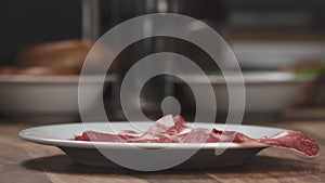 Slow motion of Italian coppa ham falling on white plate closeup