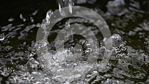 Slow motion jet of clean drinking water falls into a water tank. Drops and splashes scatter slowly close up view
