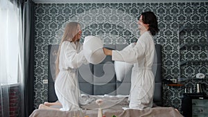 Slow motion of joyful couple in bathrobes fighting pillows and having fun in hotel room