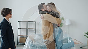 Slow motion of joyful couple buying house getting keys from realtor hugging enjoying deal