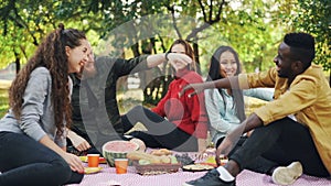 Slow motion of joyful friends African American and Caucasian doing high-five during picnic in city park. Friendship