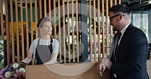 Slow motion of joyful guy paying for bunch of flowers with credit card in shop