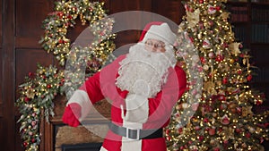 Slow motion of joyful Santa Claus dancing indoors in decorated studio with Christmas tree