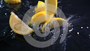 Slow motion of lemons falling with water drops on black surface.