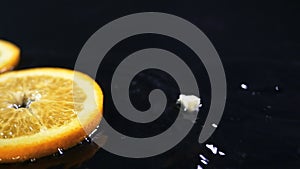 Slow motion of lemons falling with water drops on black surface.