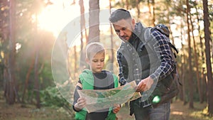 Slow motion of little boy holding map standing in forest while his father is talking and gesturing teaching his son