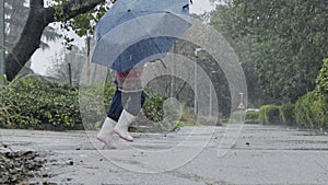 Slow motion of a little girl skipping in puddles holding an umbrella in the rain