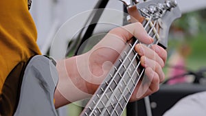 Slow motion: man hands playing bass guitar on stage of open air concert