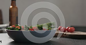 Slow motion man hands put tomatoes on top of kale in blue bowl on concrete surface photo