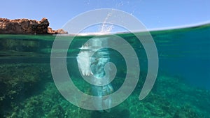 Slow motion of man jumping off cliff into the sea. Underwater