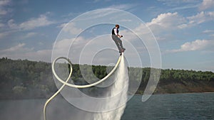 Slow motion. A man in an office suit does somersaults over the water. Flyboard as an extreme sport.