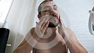 Slow motion. The man puts lotion on his face.A handsome man cares for the skin of the face, applies a moisturizing cream