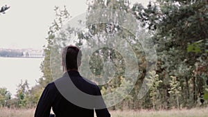 Slow motion. Man running through deep woods. Camera follows young male going out of the forest to scenic lake shore