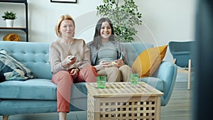 Slow motion of mature woman and teenage girl watching TV laughing pointing at screen at home