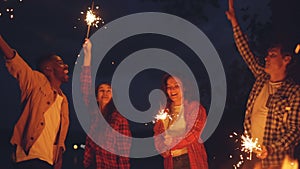 Slow motion of men and women dancing and jumping outdoors with burning sparklers, having fun, celebrating holiday and
