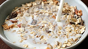 Slow motion milk pouring in bowl of muesli breakfast cereals