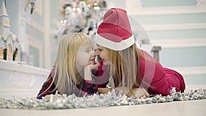 Slow motion. Mother and daughter in red dresses lie on the floor and kissing noses.
