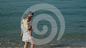 slow motion of mother holding and walking with her toddler baby girl on sea beach