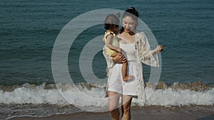 slow motion of mother holding and walking with her toddler baby girl on sea beach