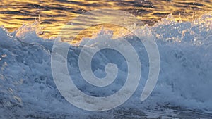 Slow motion motion shot of sea or ocean wave with golden reflections at sunset. Sea surf breaking near the shore, clean