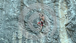 Slow motion muscular man rock climber carefully climbing on a high vertical limestone cliff