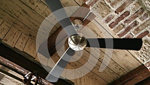 Slow motion of old ceiling fan lamp spinning in the antique interior with brick walls and wooden roof
