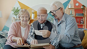 Slow motion of old men and woman watching pictures in photo album talking at home