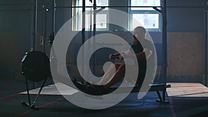 Slow motion: one man in an atmospheric fitness room in the sunlight in a rowing machine. Rower trains, cardio athlete
