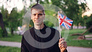 Slow motion portrain of happy englishman proud citizen waving official flag of the United Kingdom, looking at camera and