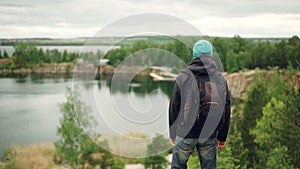 Slow motion portrait of active young man traveller with knapsack walking down the mountain and watching great view of