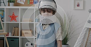 Slow motion portrait of adorable child in toy spaceman helmet standing at home and looking at camera enjoying space game