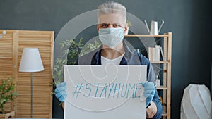 Slow motion portrait of adult man wearing mask and gloves holding stayhome poster at home